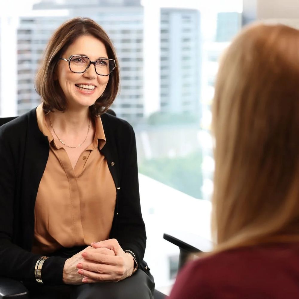 Annelie Peusschers listening to a client, with the Brisbane skyline behind her